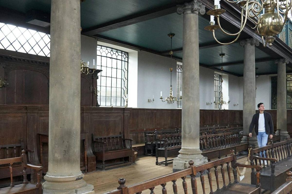 a man walking through a church with wooden pews