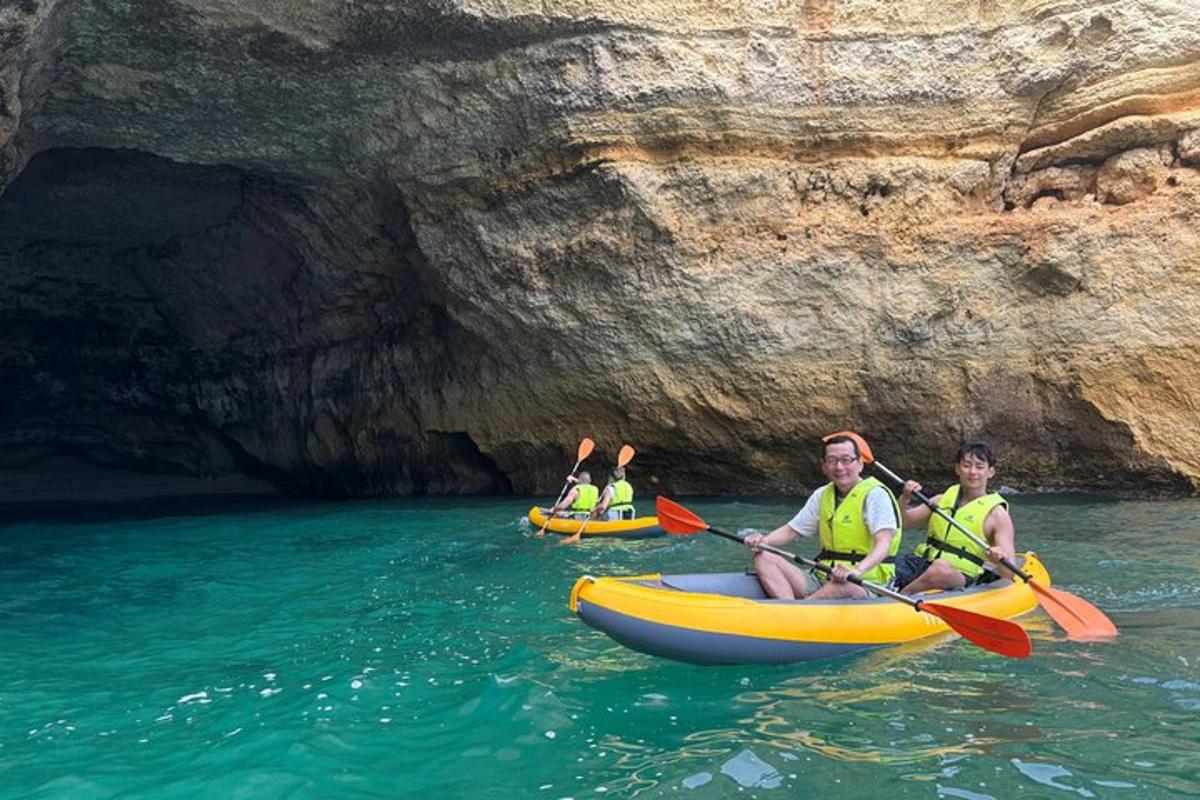 drei Personen in Kajaks im Wasser in der Nähe einer Höhle