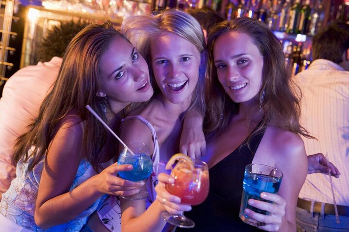três garotas posando para uma foto enquanto seguram bebidas