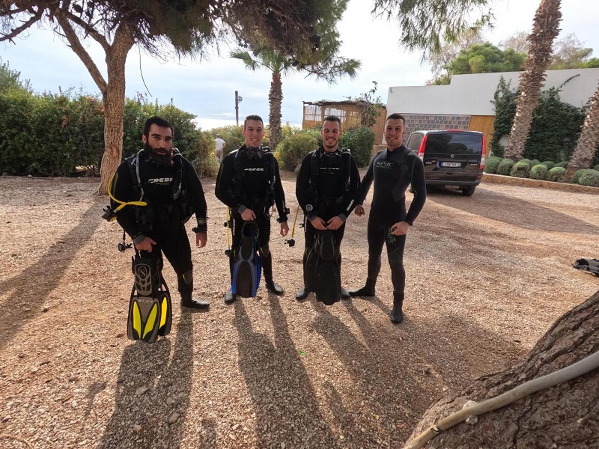 a group of men in wet suits standing on a gravel road