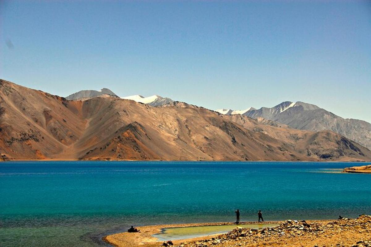 two people standing on the shore of a lake with mountains