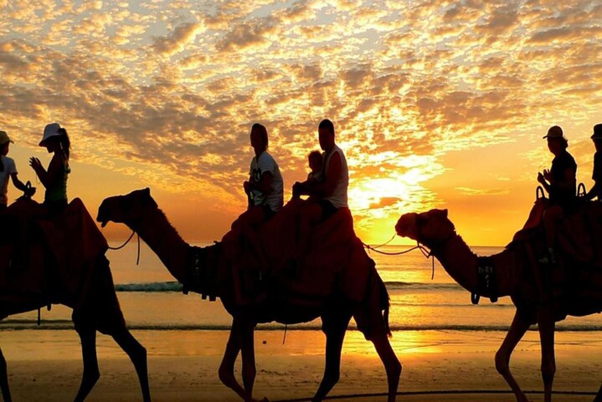 un groupe de personnes chevauchant des chameaux sur la plage au coucher du soleil