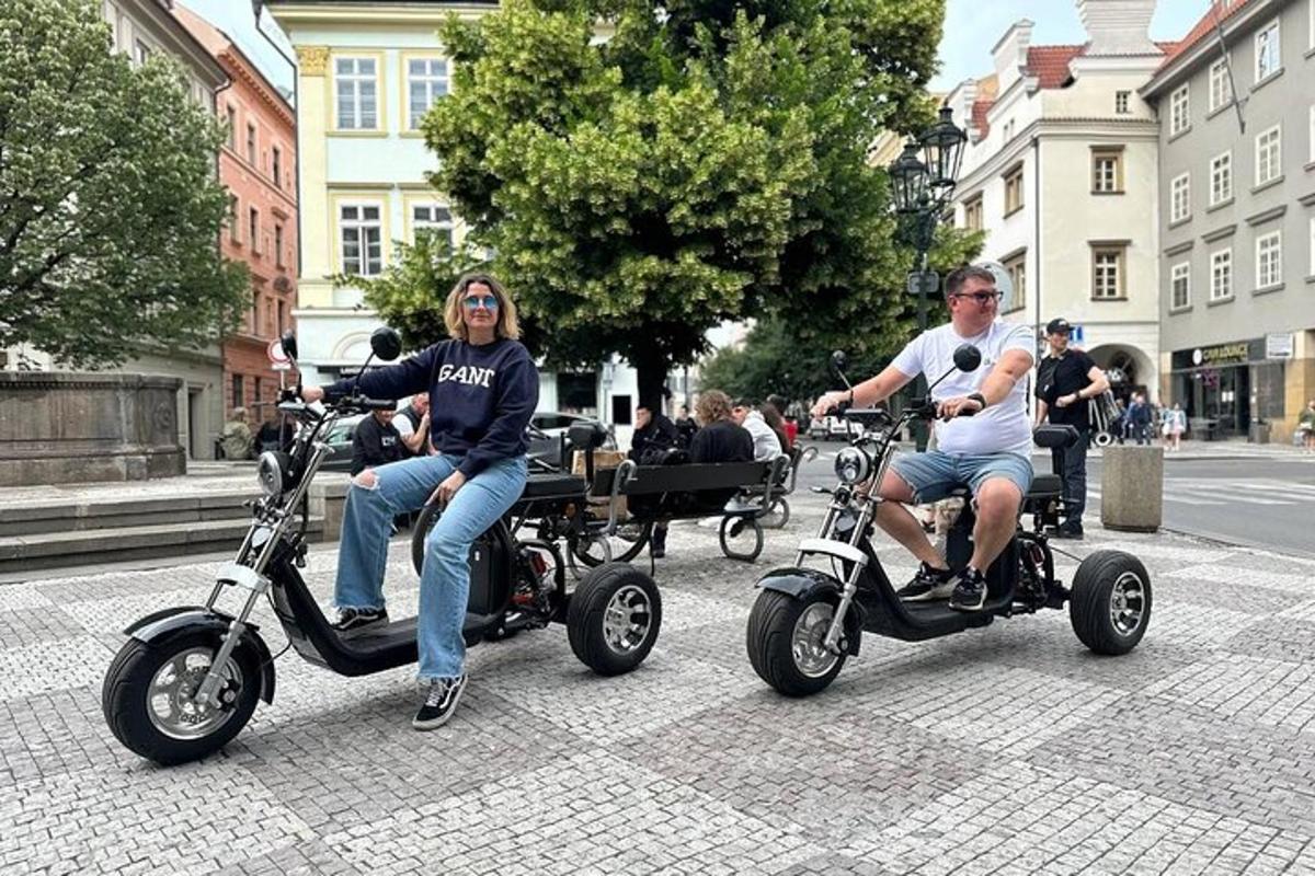 divi cilvēki brauc ar motorolleriem pa pilsētas ielu