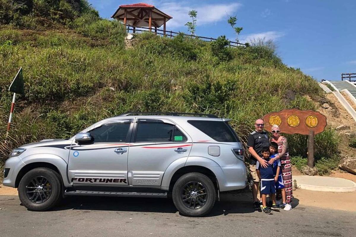 Un hombre y una familia de pie junto a un camión plateado.