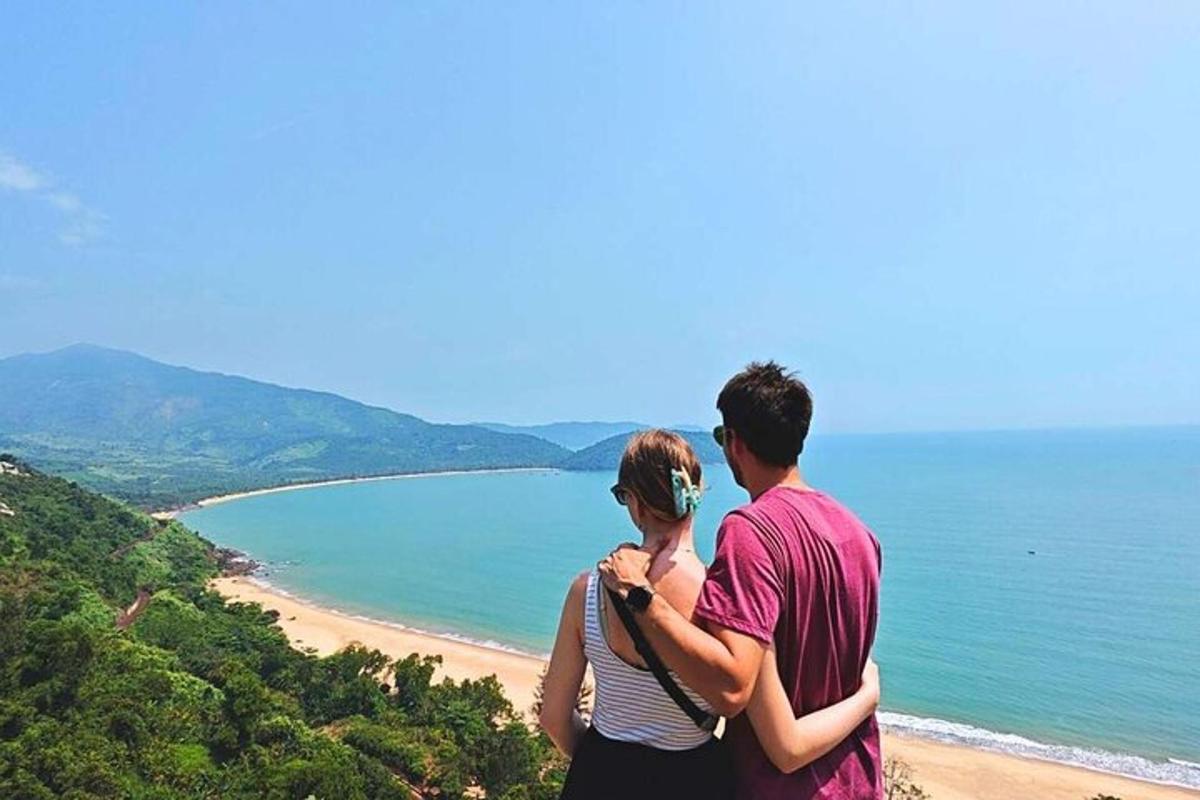 moški in ženska stojita na hribu s pogledom na plažo