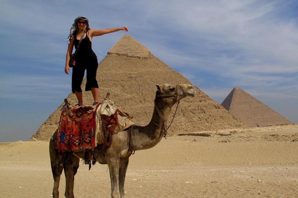 en kvinne som står på en kamel foran pyramider