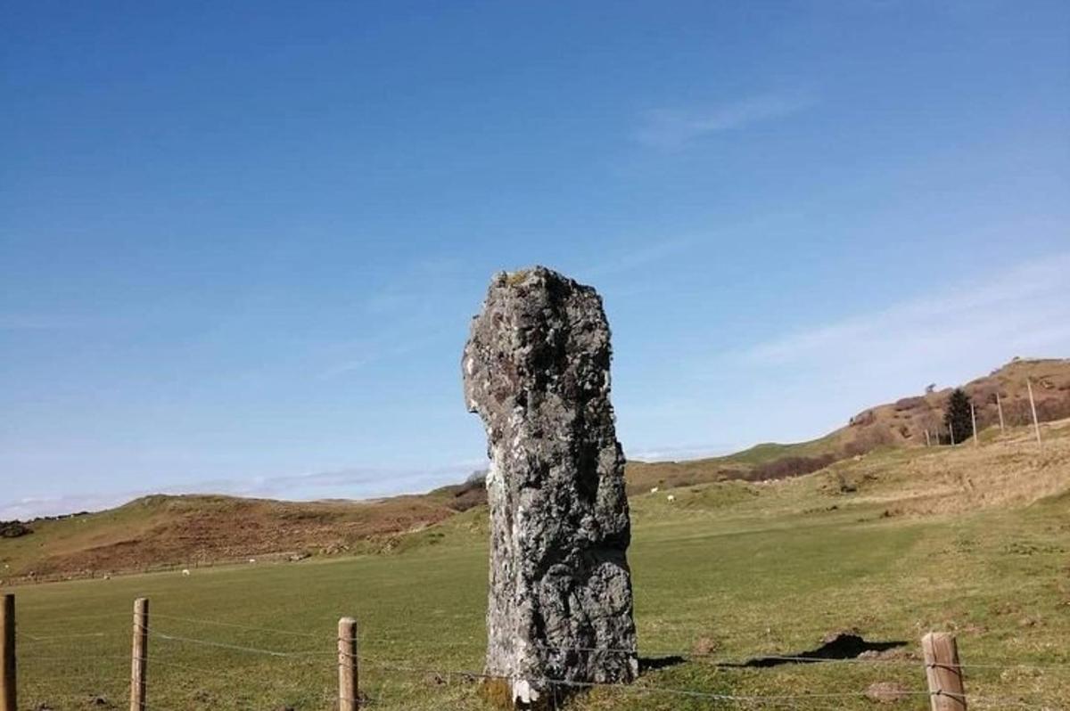 a rock pillar in a field with a fence