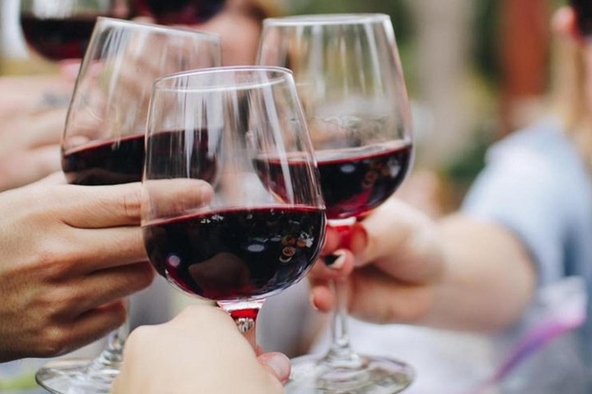 three people are holding up glasses of red wine