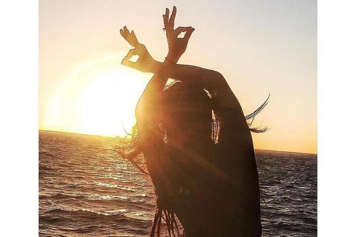 a woman standing in the ocean with the sun in the background