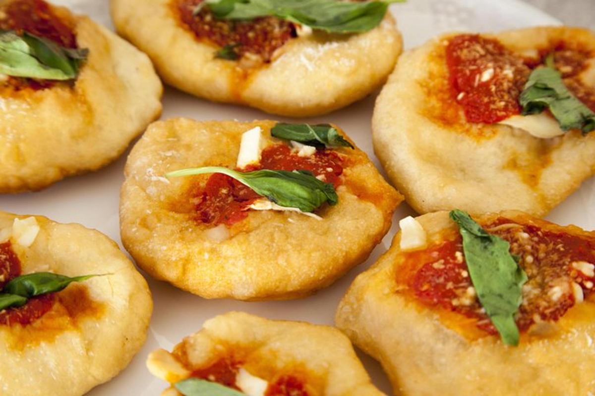 Un grupo de pizzas pequeñas con salsa y albahaca encima.