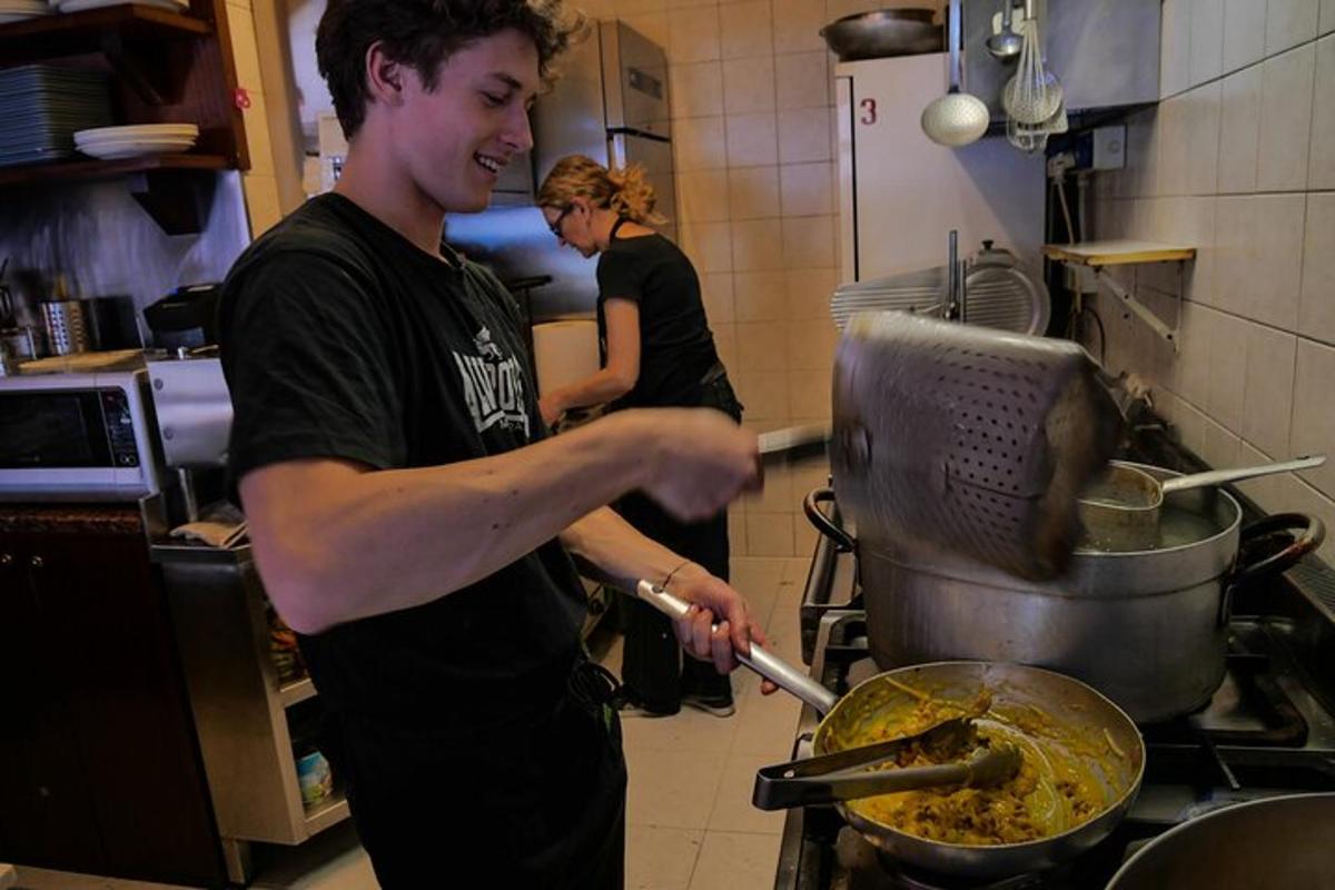 un home a la cuina preparant menjar en una paella