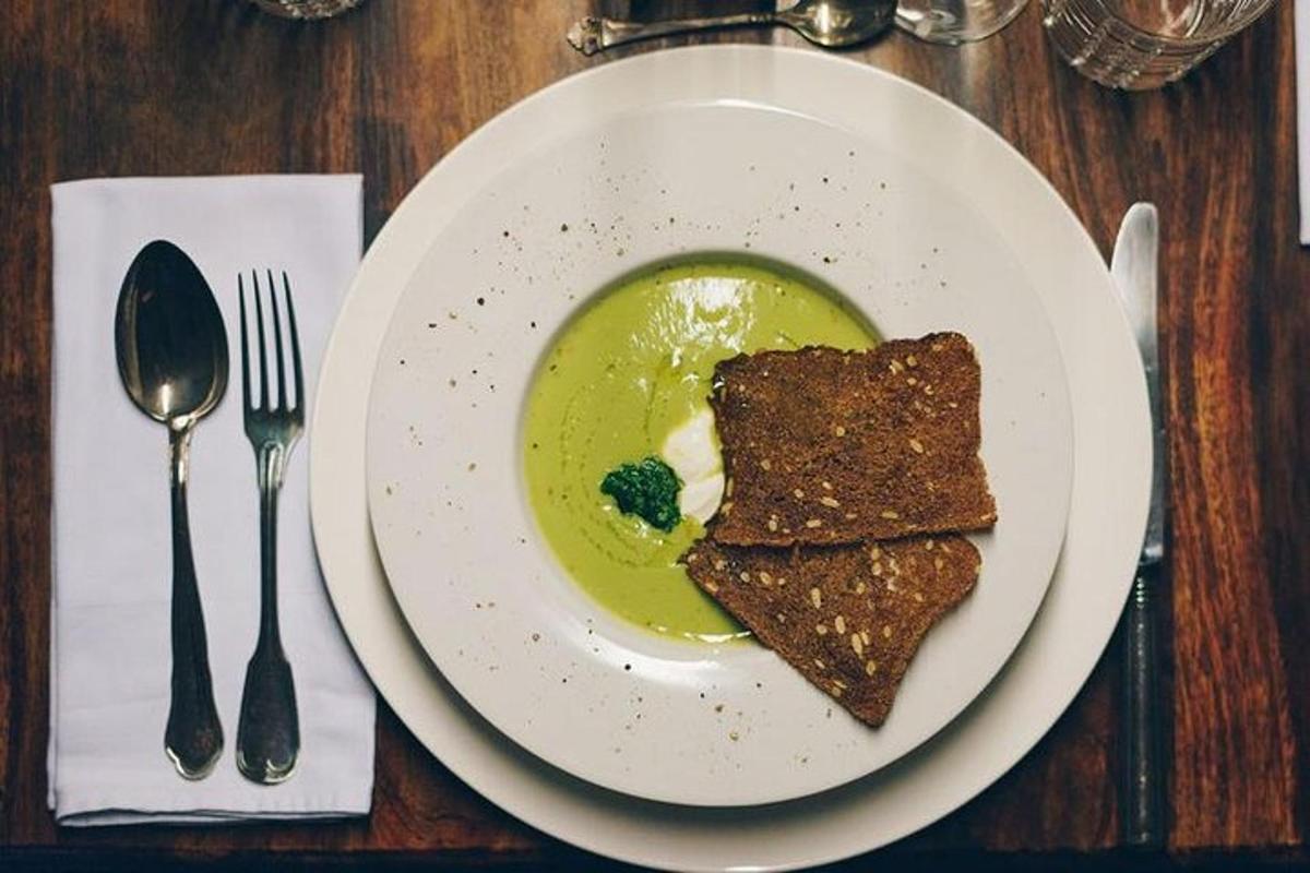 a white plate with a bowl of soup with broccoli