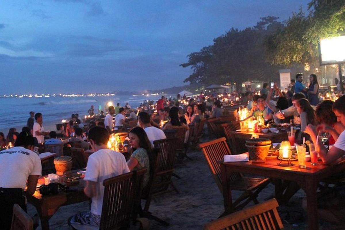 một đám đông người ngồi ở bàn trên bãi biển vào ban đêm