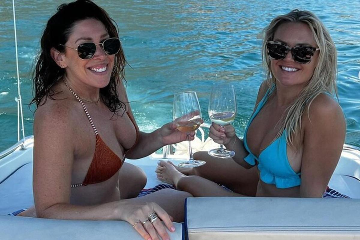due donne in costume da bagno sedute su una barca con bicchieri di vino