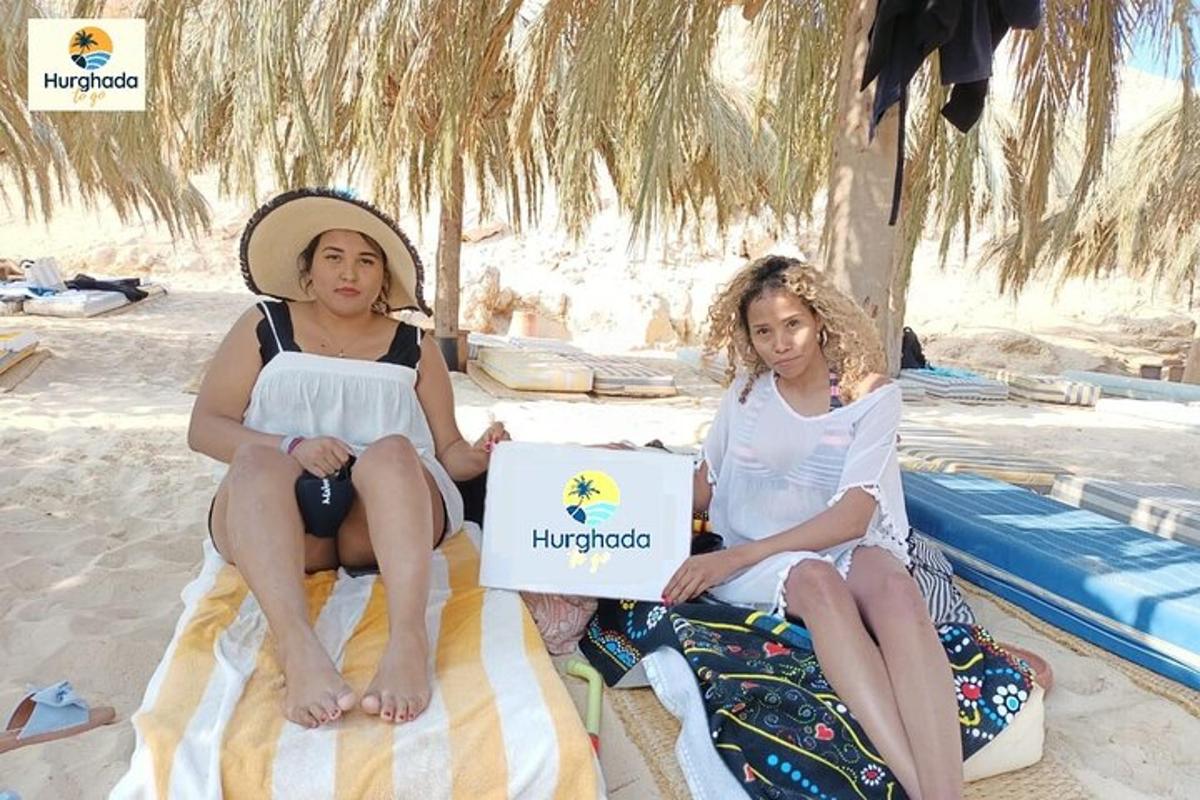 two girls sitting on the beach with a laptop
