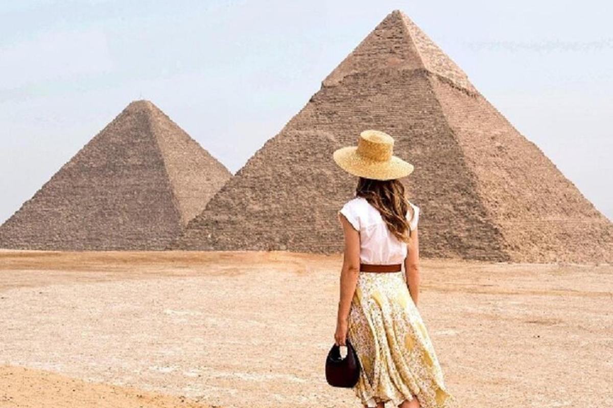a woman in a hat standing in front of the pyramids