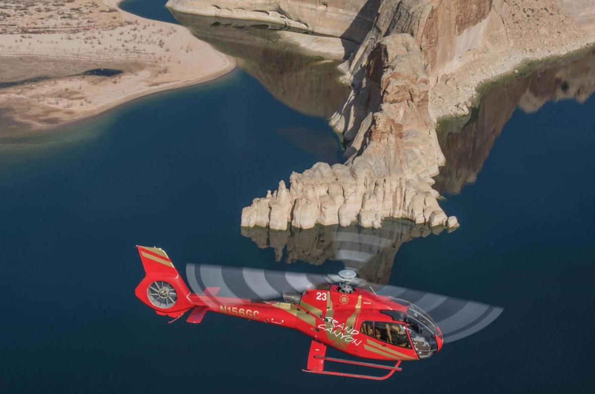 rdeč helikopter leti nad vodo ob pečini