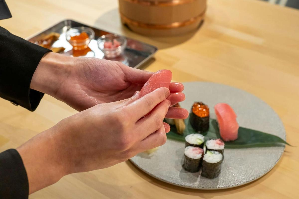 seseorang yang memegang sekeping makanan di sebelah pinggan sushi