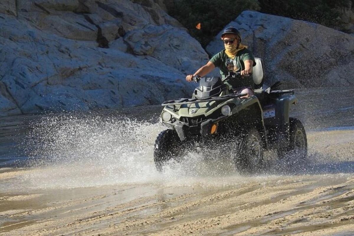 un home que condueix un quad per la platja