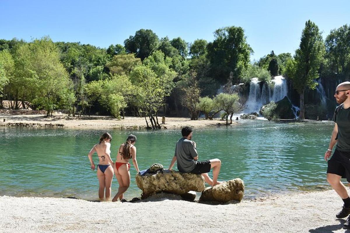 a group of people standing on the beach near a waterfall
