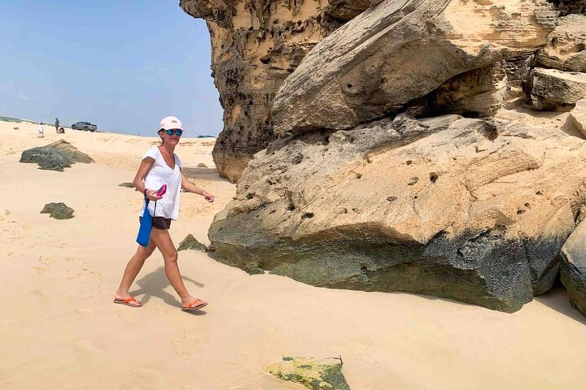 a woman walking on the beach near some rocks