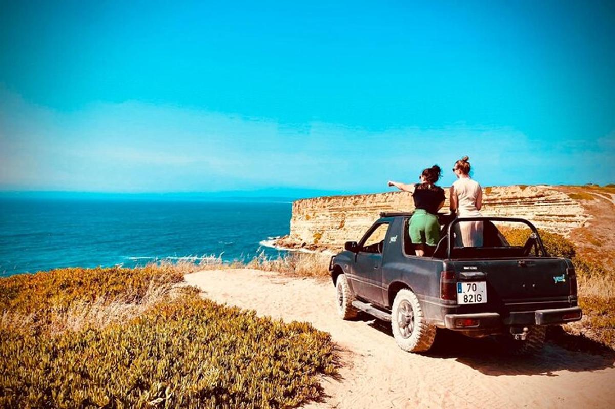 two people standing on top of a truck on a dirt road