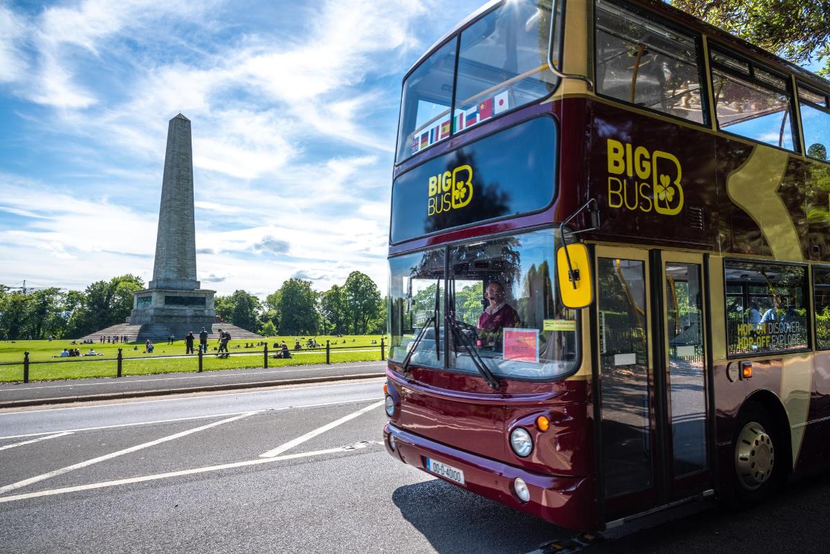 a double decker bus driving down a road in front of a monument