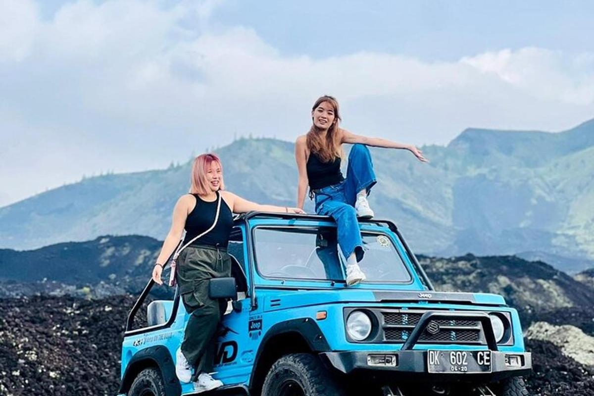 dvě ženy sedící na střeše modrého džípu