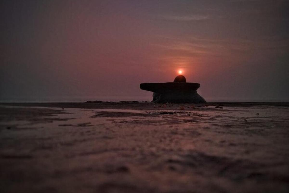 un banc a la platja amb una posta de sol al fons