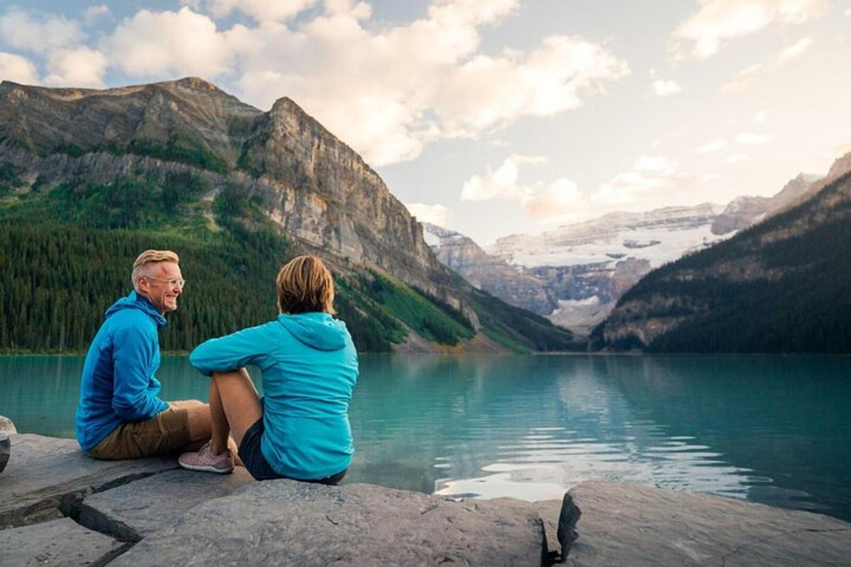 a man and woman sitting on a rock near a lake