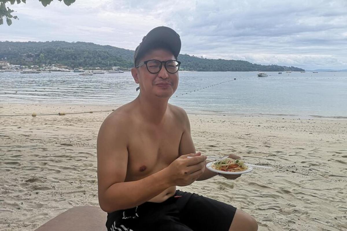 um homem sentado na praia com um prato de comida
