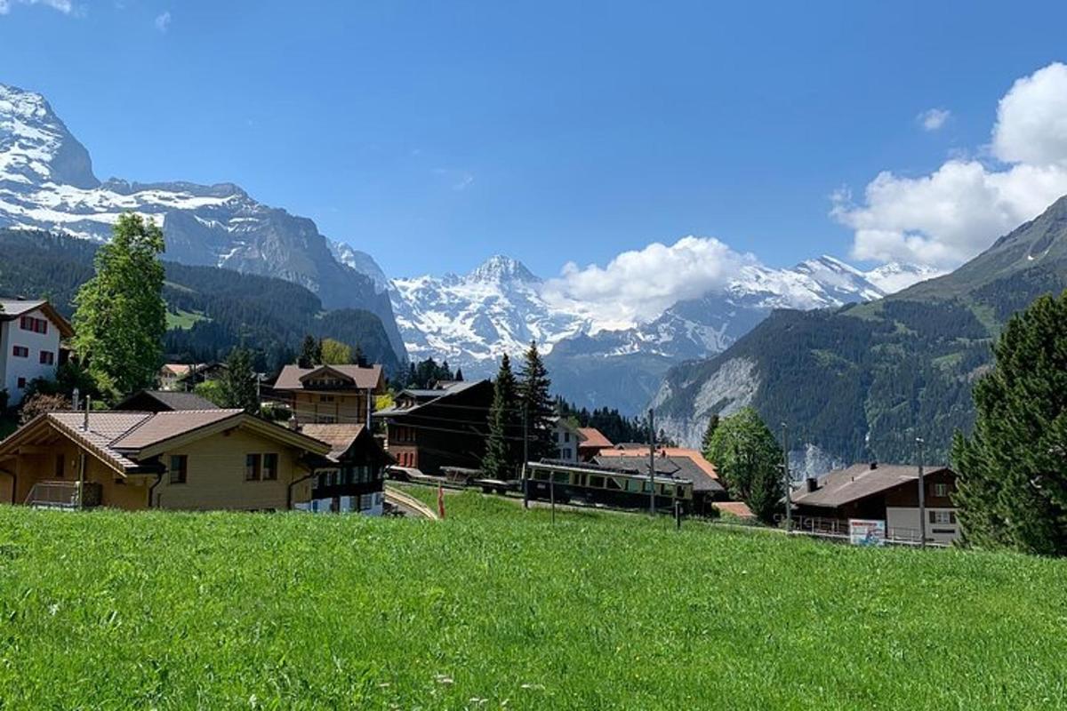 una collina verde con un villaggio e montagne sullo sfondo