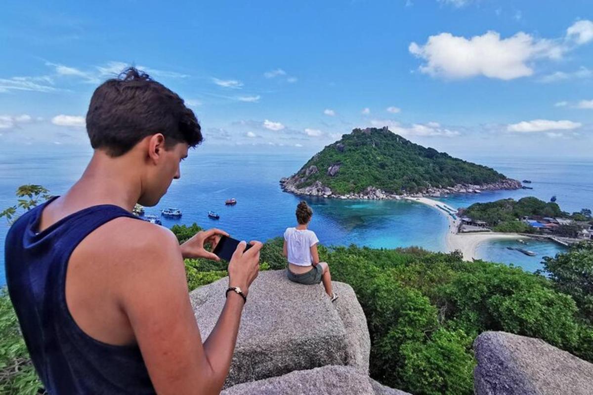 un uomo seduto su una roccia che scatta una foto dell'oceano