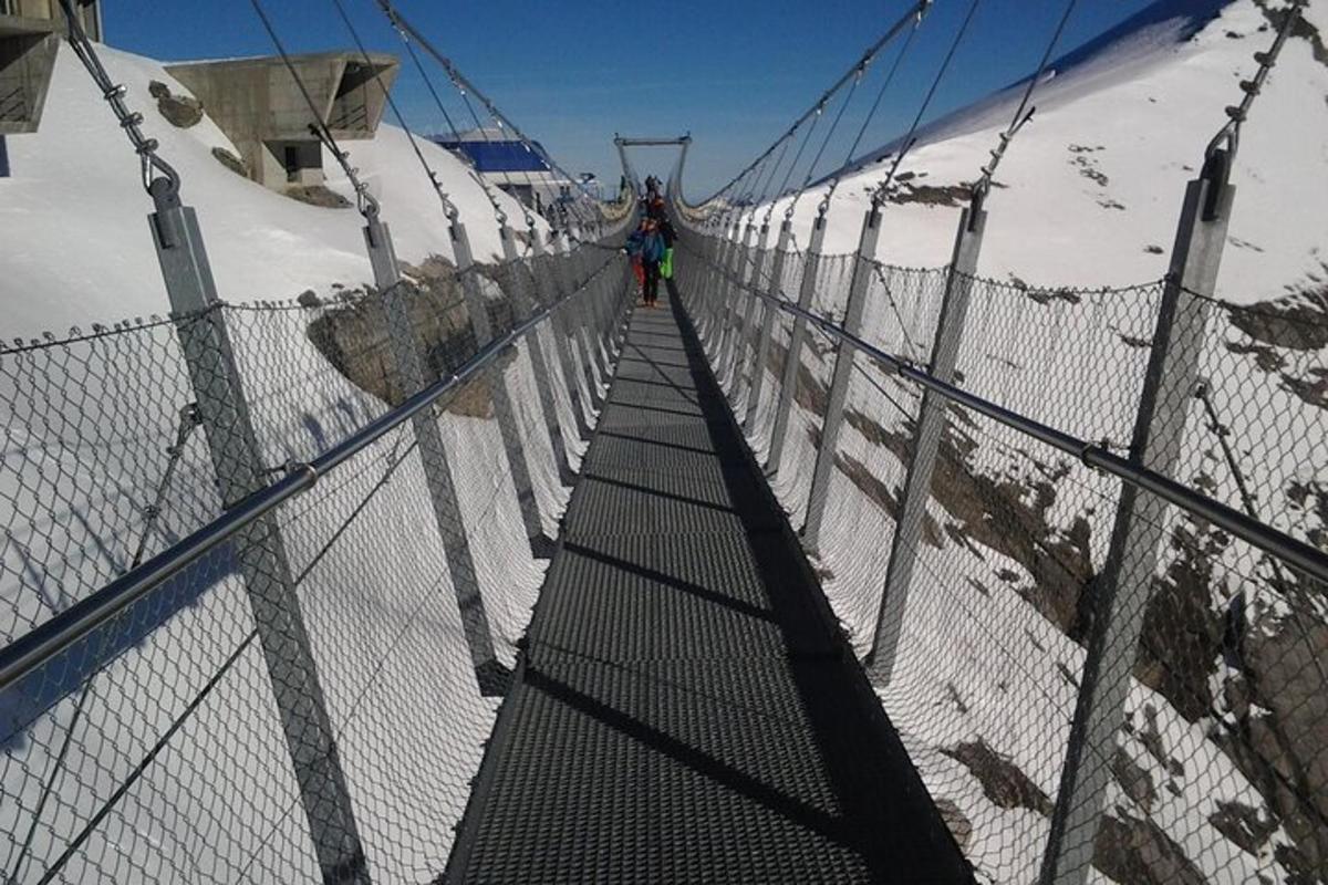 una persona caminant per un pont penjant sobre una muntanya coberta de neu