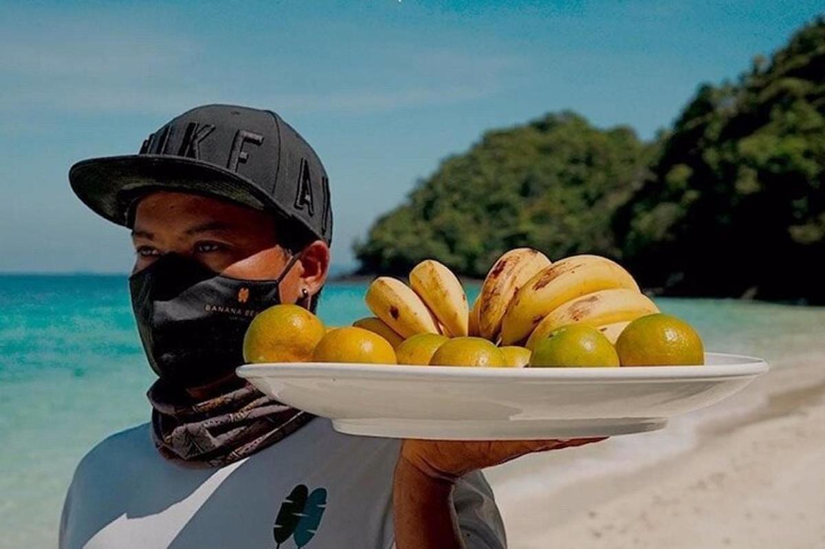 en mann som holder en tallerken med frukt på stranden
