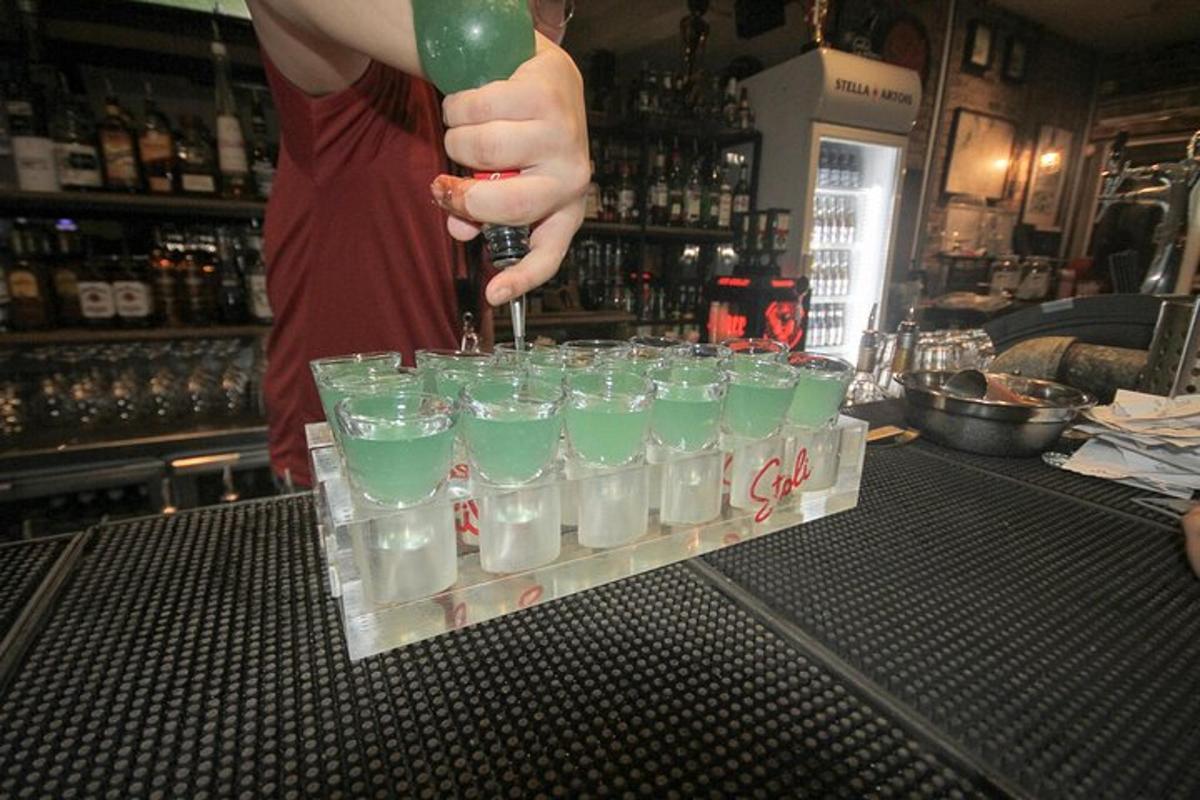 osoba nalévá zelenou tekutinu do skupiny sklenic