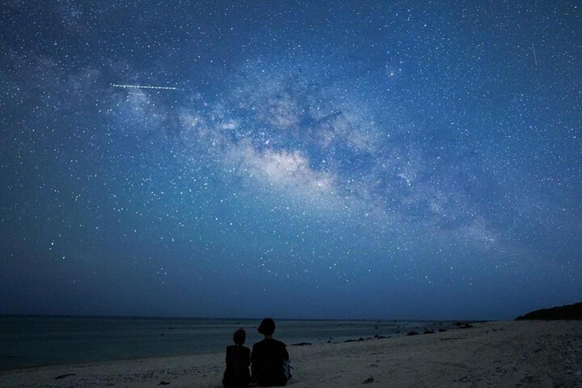 two people sitting on the beach looking at the universe