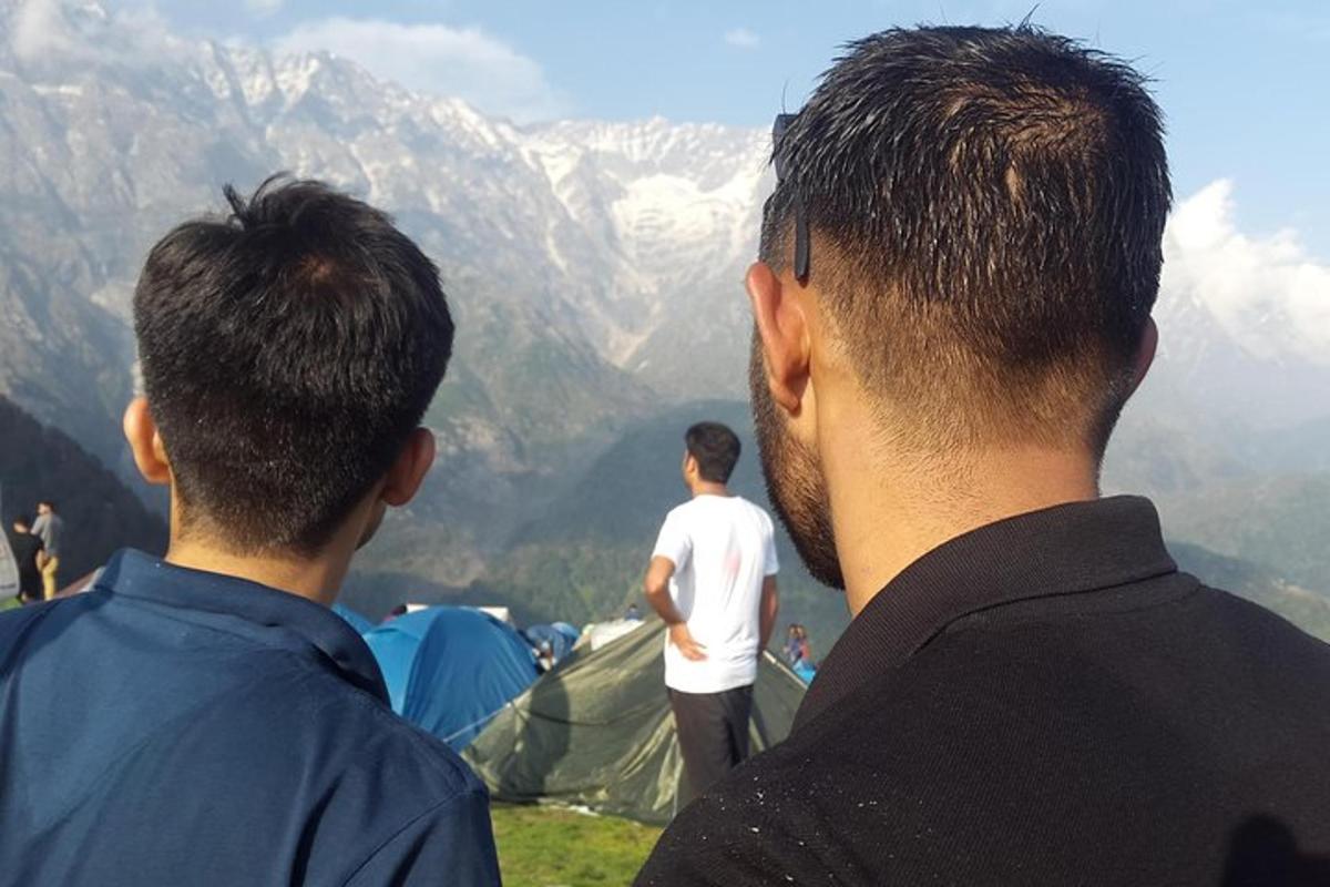 two men standing on top of a hill looking at a mountain