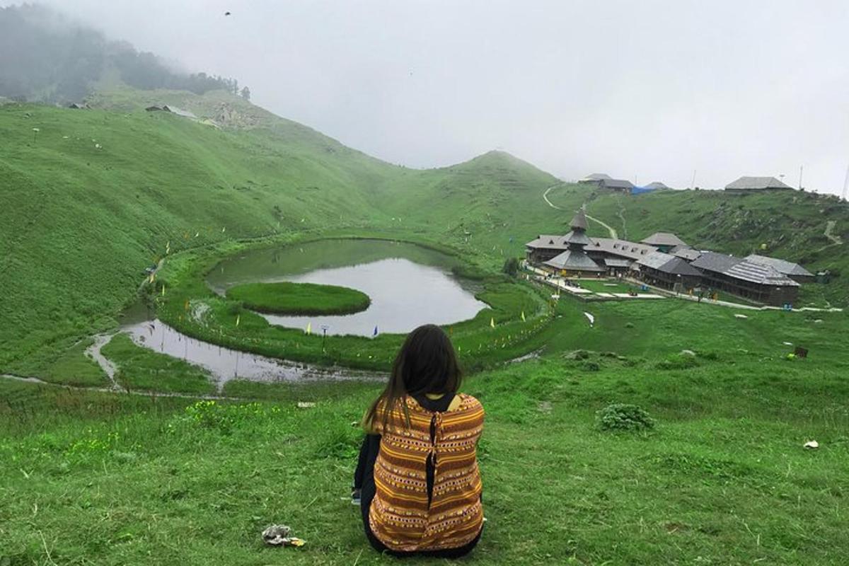 a woman sitting on a hill looking at a lake