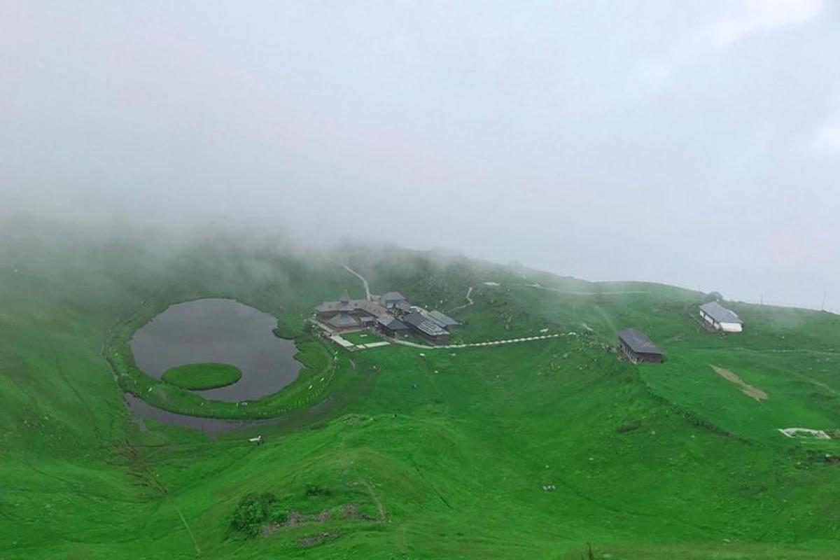 a house on top of a green hill with a lake