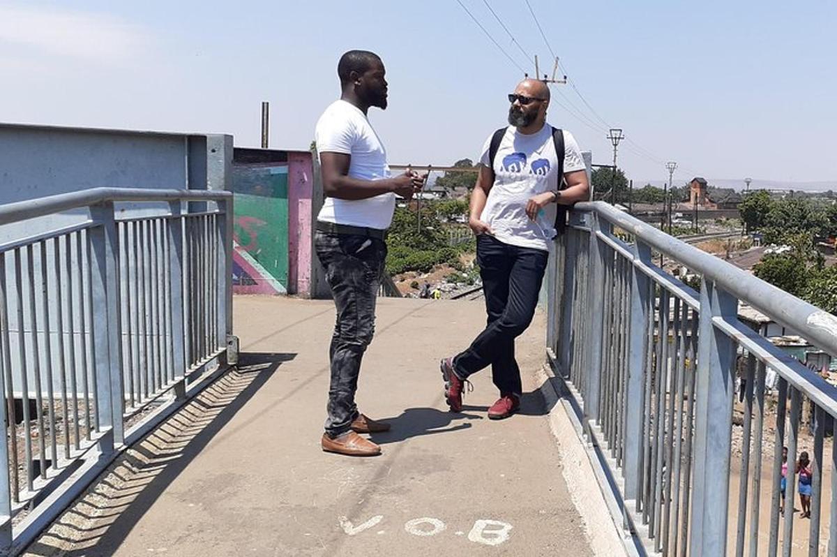 two men standing on a bridge looking at their cell phone