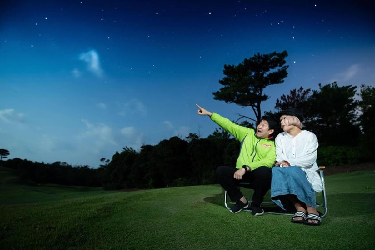 two people sitting on a chair on a field at night