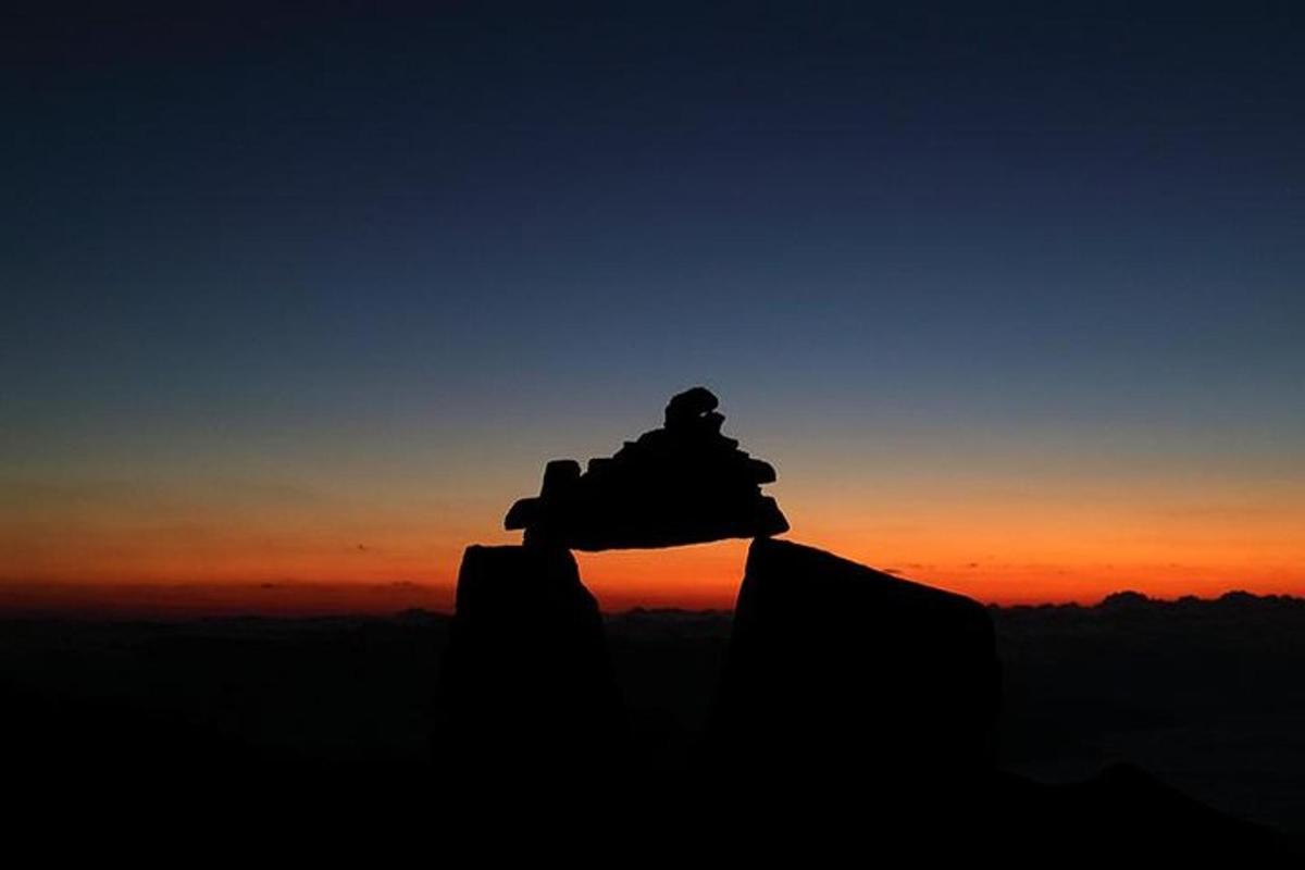 uma pessoa sentada em uma rocha ao pôr do sol