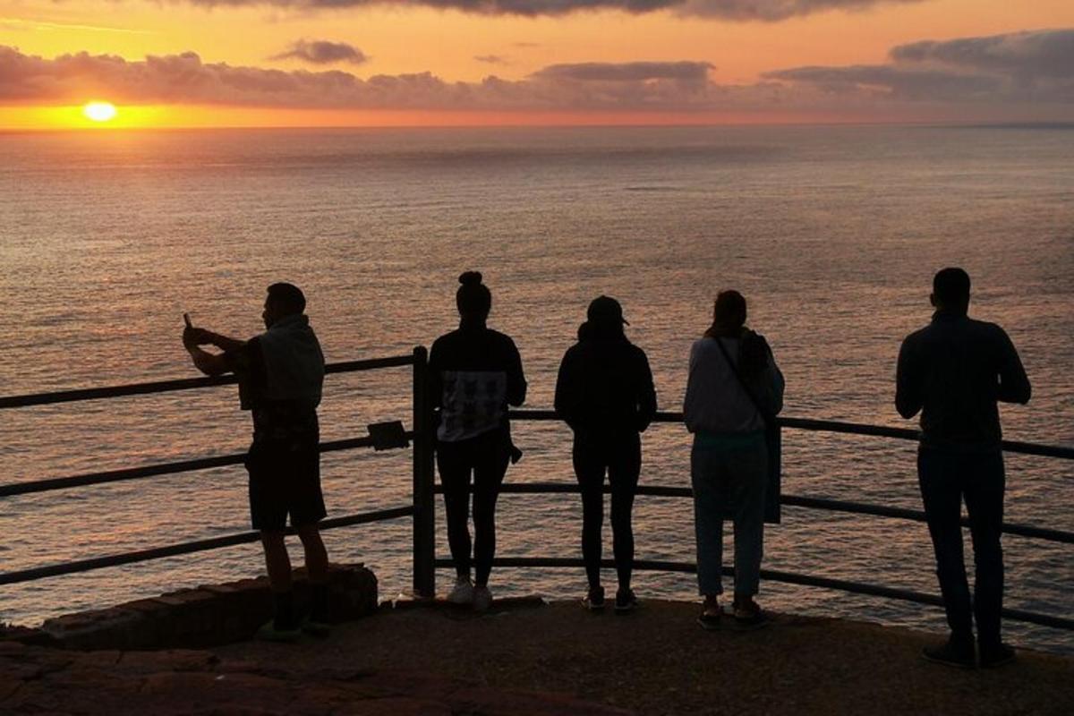 Un grupo de personas de pie en un muelle mirando la puesta de sol