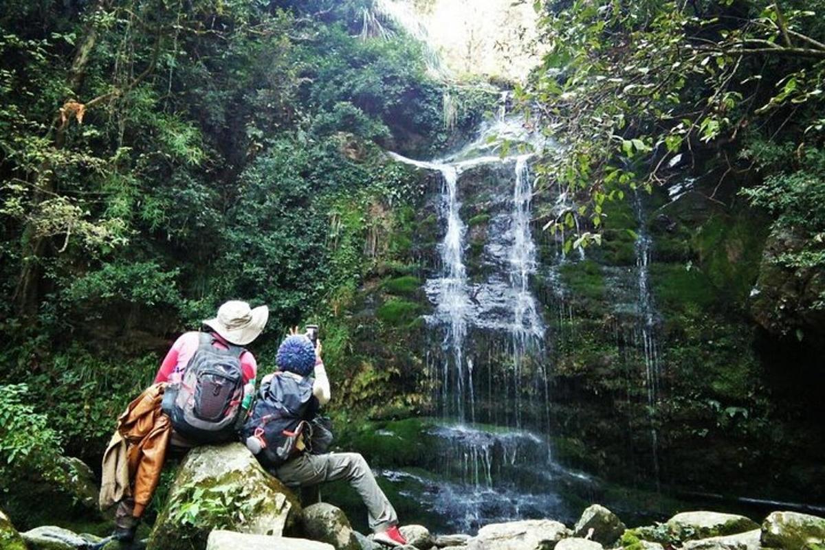 two people sitting on a rock in front of a waterfall