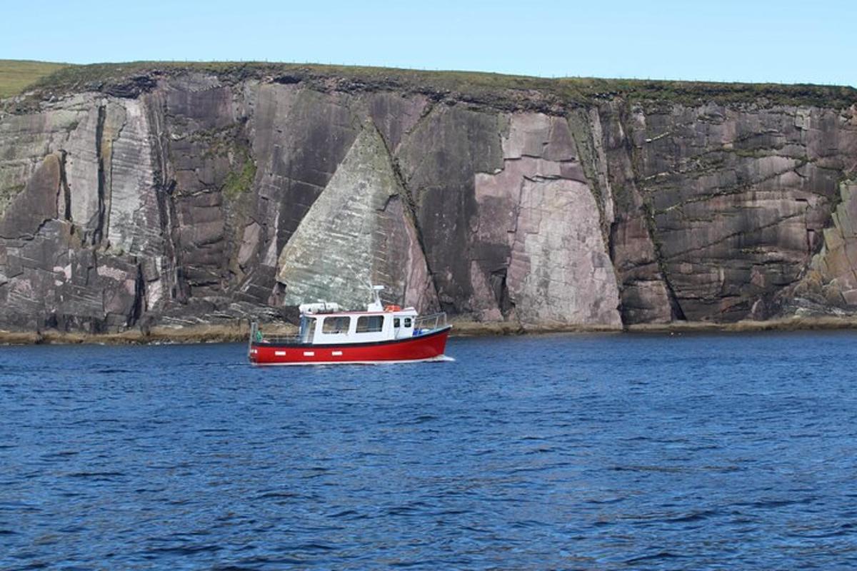 a red boat in the water next to a cliff