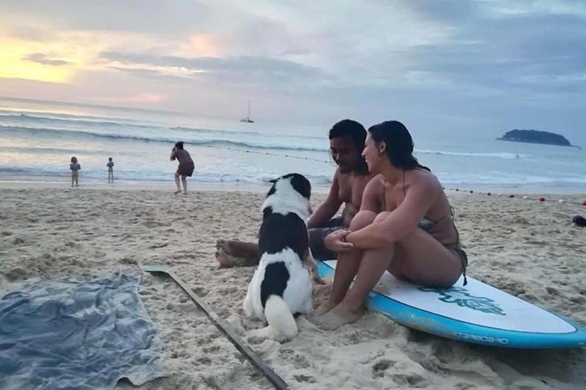 due persone e un cane seduti su una tavola da surf sulla spiaggia