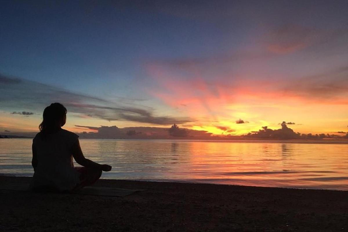 a woman sitting on the beach watching the sunset