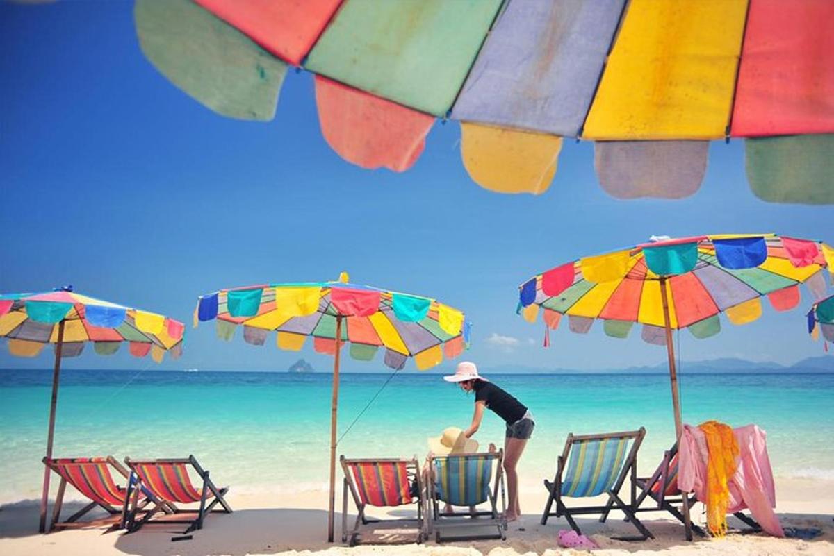 Un hombre parado en una playa con sillas y sombrillas.