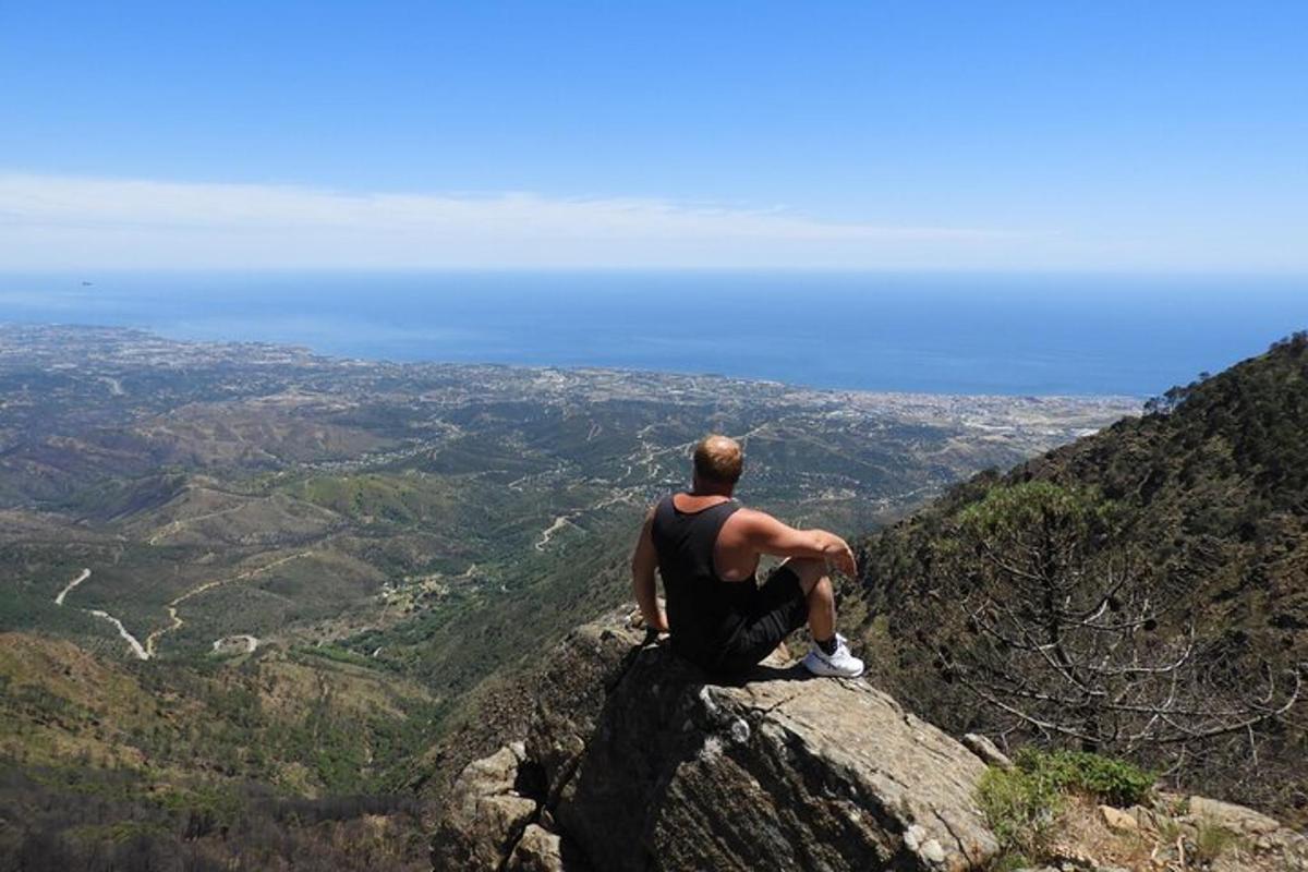 un home assegut a dalt d'una roca mirant una vall
